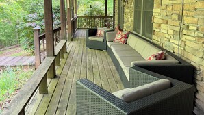A covered porch with a stone wall, wooden deck, wicker furniture, and a bench.