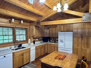 A wooden kitchen with a central island, a built-in dishwasher, and a refrigerator. - Cozy Waterfront Log Cabin Retreat on a Quiet Creek (Mineral)