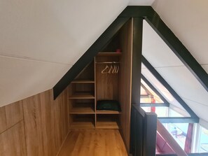 Ein Holzinnenraum mit schrägem Dach, einem Kleiderschrank mit Ablagefläche und Blick durch ein Fenster.