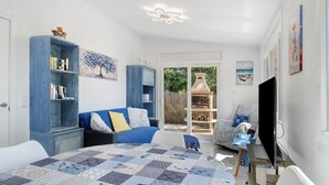 A bedroom with a bed, a blue sofa, a bookshelf, a TV, and a view of the outdoors. - Villa “My Little Castle Platja D'Aro” with Sea View, Balcony and Wi-Fi (Castell d'Aro)