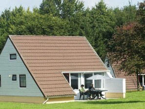 Ein eingeschossiges Haus mit geneigtem Dach, einer Veranda mit weißer Brüstung und einer kleinen angebauten Garage.