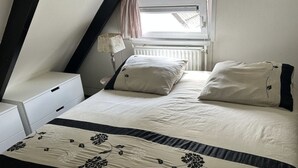 A bedroom with a bed, a nightstand, a lamp, and a window with curtains. - Bungalowpark Simpelveld - Alpha 89 by Interhome (Simpelveld)