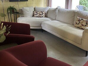 Ein Wohnzimmer mit einem beigefarbenen Ecksofa, einem roten Sessel und einem kleinen Beistelltisch mit einer Pflanze.