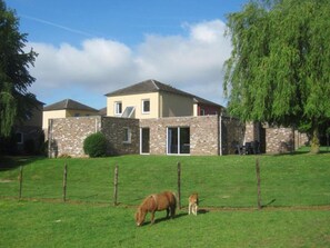 Ein zweistöckiges Haus mit Natursteinfassade, einem eingezäunten Garten und einem Baum.