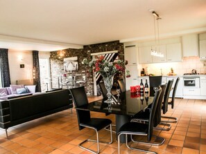 Ein modernes Wohnzimmer mit einer schwarzen Couch, einem Esstisch mit Stühlen und einer Küchenzeile mit weißen Schränken und Fliesenboden.