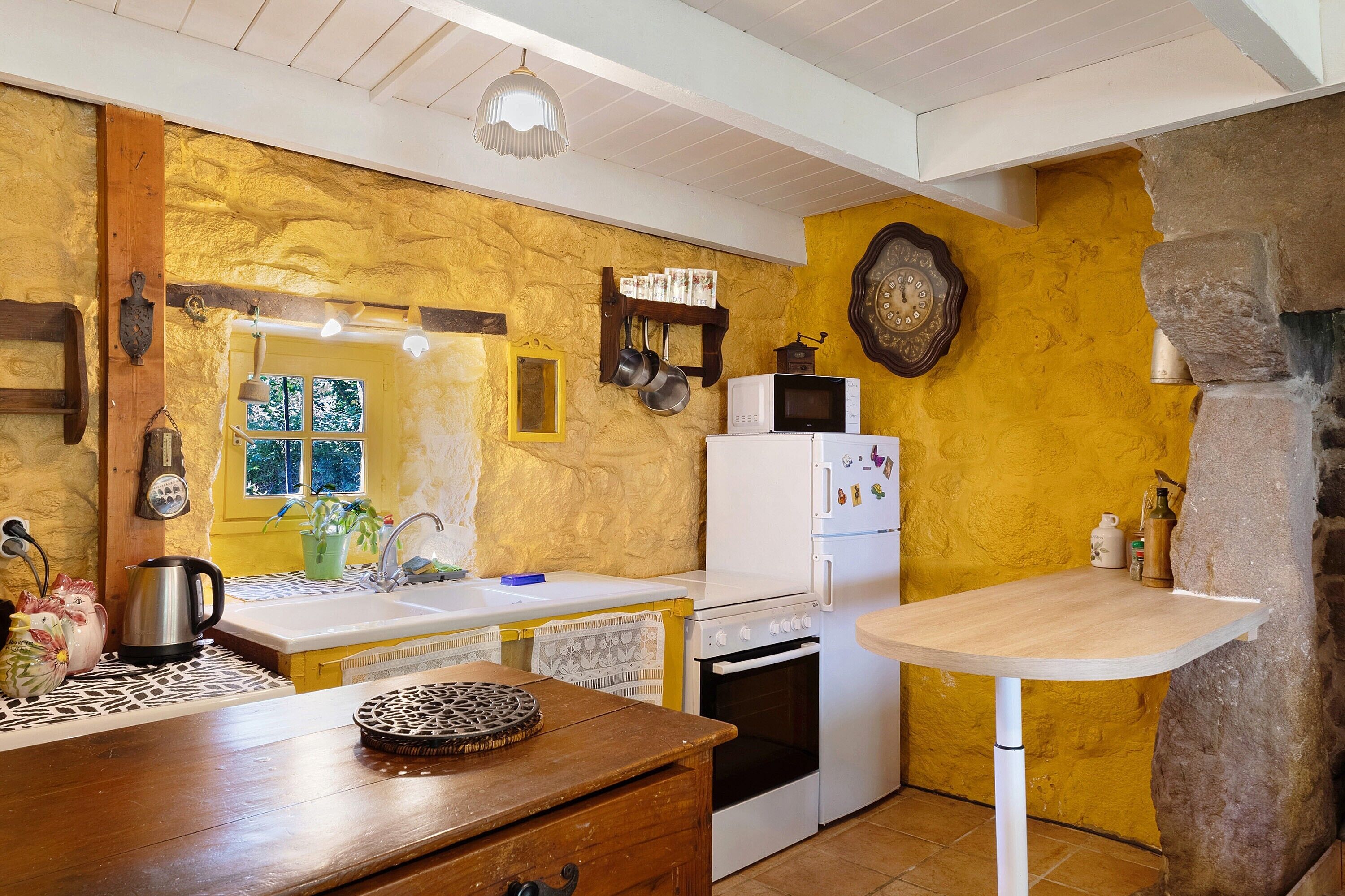 A kitchen with a stone wall, wooden cabinets, a white refrigerator, a stove, and a window with a view.