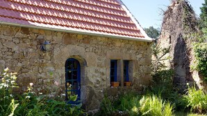 A stone building with a red-tiled roof, a blue door, and windows with blue shutters.