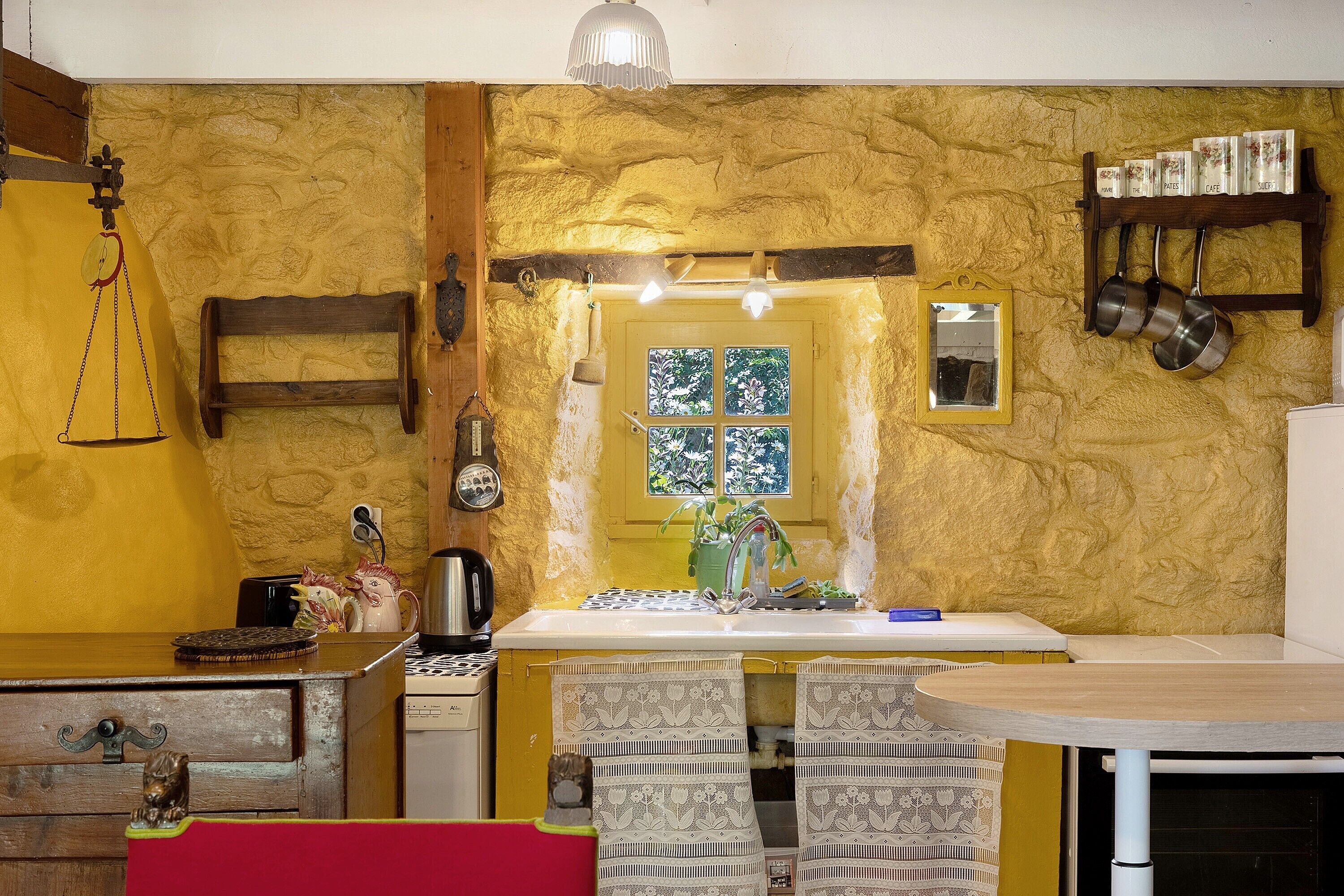 A kitchen with a stone wall, a wooden table, a sink, and hanging pots.