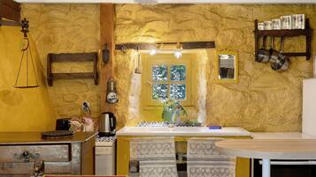 A kitchen with a stone wall, a wooden table, a sink, and hanging pots.