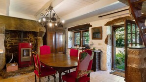 A dining area with a stone fireplace, a red wood-burning stove, and a large wooden table with red upholstered chairs.