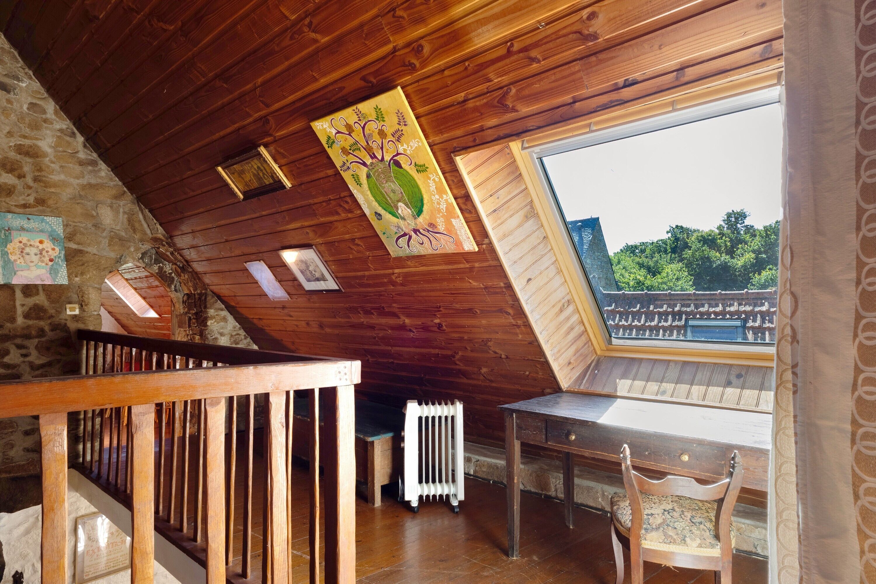Techo de madera con diseño inclinado, una ventana con vista a un balcón y una mesa con una silla.