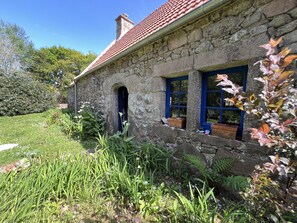 Une maison en pierre avec un toit recouvert de tuiles rouges, une petite fenêtre en arc de cercle et une fenêtre à cadre bleu.