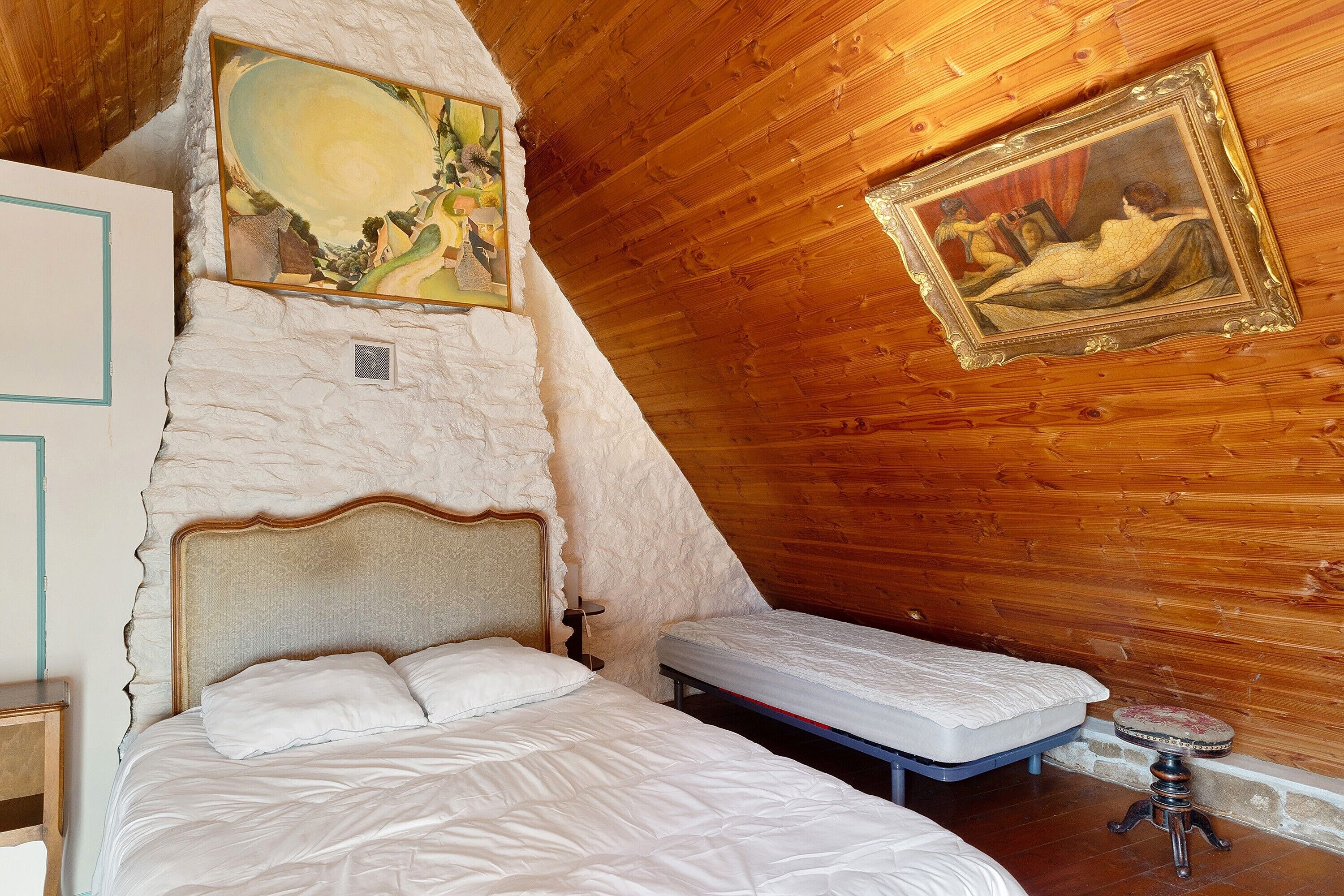 A bedroom with a large bed, a smaller bed, a wooden ceiling, and two paintings on the walls.