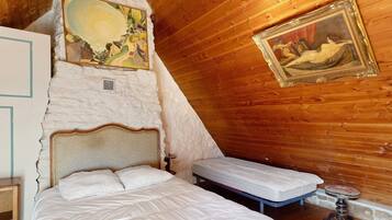 A bedroom with a large bed, a smaller bed, a wooden ceiling, and two paintings on the walls.