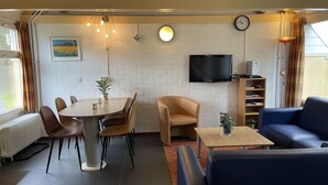 Ein Zimmer mit Esstisch, Stühlen, einer Couch, einem Fernseher und einem Bücherregal.