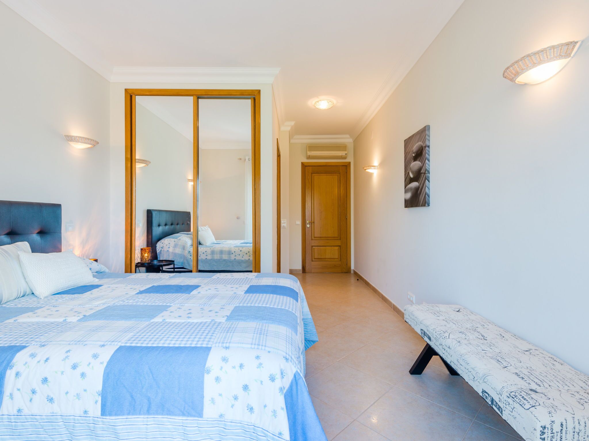 A bedroom with a bed, bedside table, lamp, and a bench.