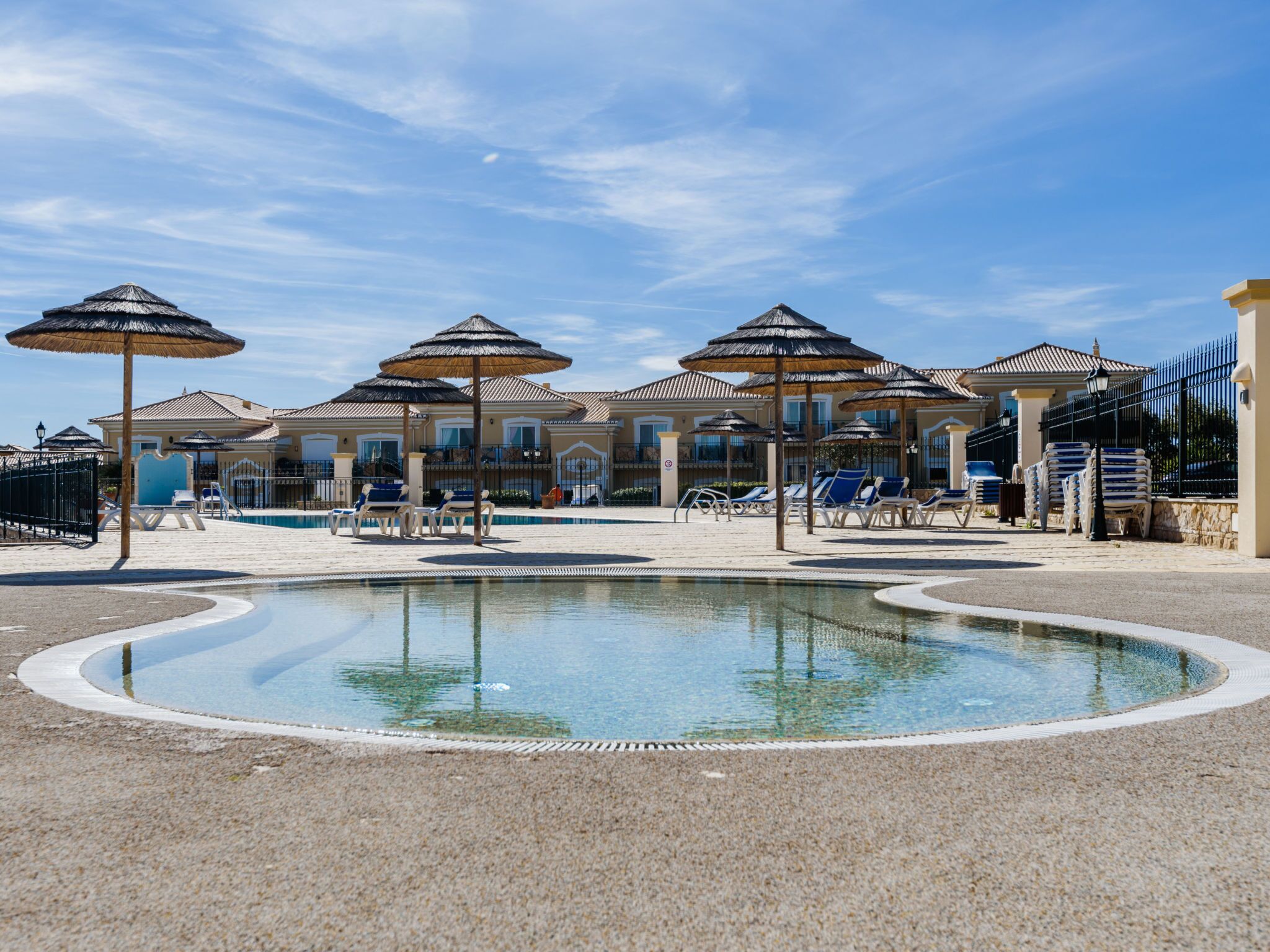 A pool area with lounge chairs and umbrellas, surrounded by a building with a tiled roof.