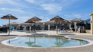 Ein Poolbereich mit Liegestühlen und Sonnenschirmen, umgeben von einem Gebäude mit einem Ziegeldach.