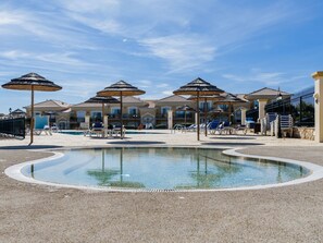 A pool area with lounge chairs and umbrellas, surrounded by a building with a tiled roof. - Apartment  by Interhome (Lagos)
