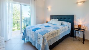 Ein Schlafzimmer mit einem großen Bett, einer Glasschiebetür zu einem Balkon und einem kleinen Tisch mit einer Lampe.
