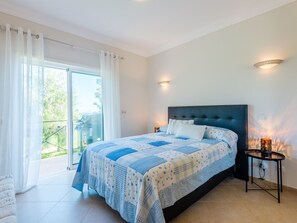 A bedroom with a large bed, a sliding glass door to a balcony, and a small table with a lamp. - Apartment  by Interhome (Lagos)