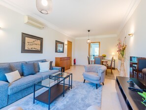 A modern living room with a sofa, armchair, and coffee table. There is a dining area with a table and chairs, and a kitchen in the background. - Fairviews Village - Boavista Resort in Lagos by Interhome (Lagos)