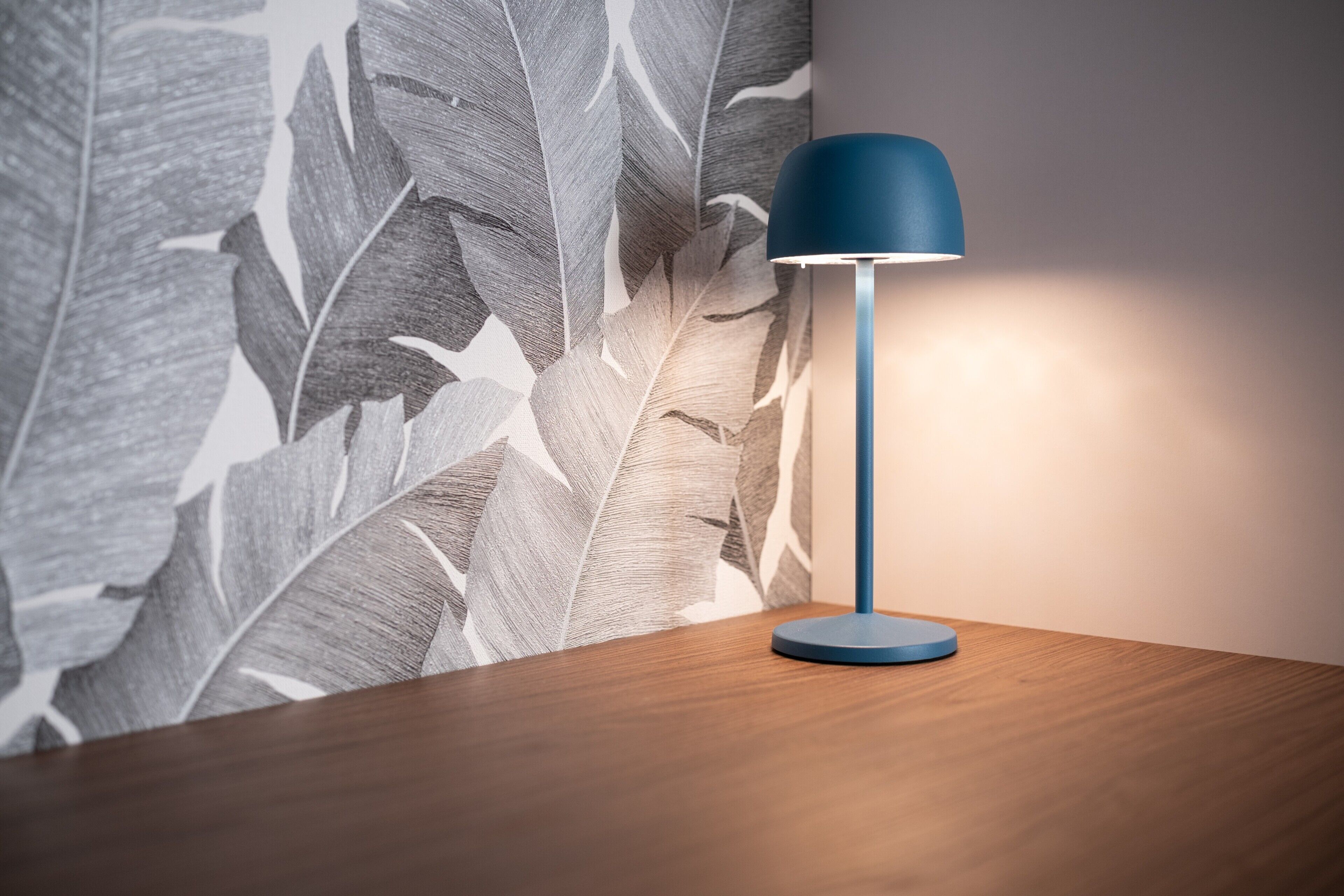 Ein Tisch mit einer blauen Lampe, eine Wand mit Blattmuster und eine Holzoberfläche.