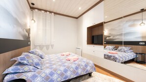 A bedroom with a bed, a mirror, a window with curtains, and a ceiling with wooden beams.
