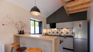 A modern kitchen with a central island, bar stools, a refrigerator, and a decorative wall piece. - Grand Gîte Les Hangars: South-Facing Terrace, 4 Bedrooms, Sauna & Whirlpool – Beds Made, Cleaning Included (Saulxures-sur-Moselotte)