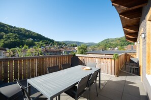 A patio with a table and chairs, a wooden fence, and a view of a hillside with houses.
