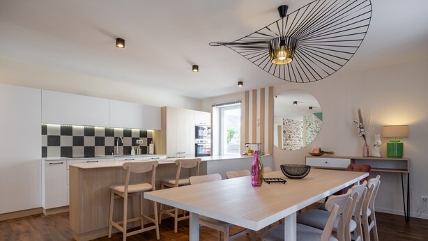 Una cucina moderna con isola centrale, mobili bianchi e zona pranzo con tavolo e sedie bianche.