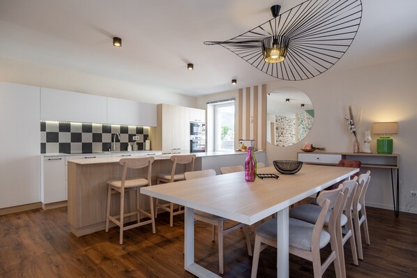 A modern kitchen with a central island, white cabinetry, and a dining area with a white table and chairs.