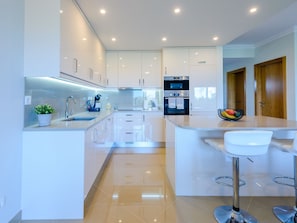 Een moderne keuken met witte kasten, een centraal eiland met barkrukken en inbouwapparatuur.