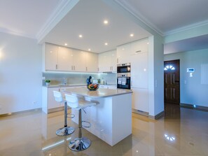 A modern kitchen with white cabinetry, a central island with bar stools, and built-in appliances. - Boavista Golf and Spa Resort - Bayview by Interhome (Lagos)