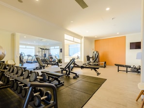 Ein Fitnessstudio mit verschiedenen Trainingsgeräten, darunter Laufbänder, Kraftgeräte und Kurzhanteln.