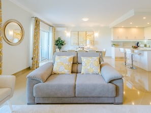 Ein modernes Wohnzimmer mit grauem Sofa, einem Essbereich und einer Küche.