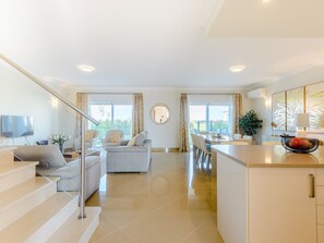 A modern living room with a sofa, a dining area with chairs, a kitchen counter, and a staircase. - Boavista Golf and Spa Resort - Bayview by Interhome (Lagos)