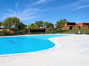 A swimming pool with a curved edge, surrounded by a paved area and a fence. - Apartment  by Interhome (Quarteira)