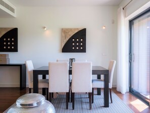 A dining area with a table and chairs, a decorative wall piece, and a large window. - Apartment  by Interhome (Quarteira)