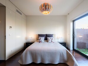 A bedroom with a large bed, two bedside tables, a modern pendant light, and a sliding glass door leading to an outdoor area. - Apartment  by Interhome (Quarteira)