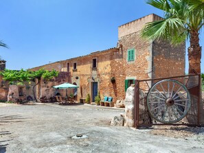 Un espacio al aire libre con mesas y sillas, una palmera y un edificio rústico con una noria grande.