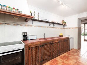 Cocina con estufa, cafetera y lavaplatos. Hay repisas sobre la encimera con varios objetos.