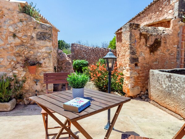 Un área de estar al aire libre con una mesa de madera y un banco, rodeada de muros de piedra y plantas en macetas.