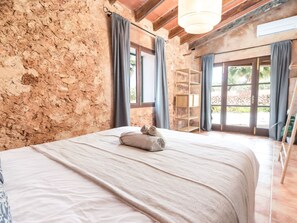 A bedroom with a stone wall, a bed with a rolled towel, and a wooden shelf. - Casa Antigua by Interhome (Santanyí)