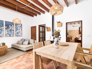 A spacious living area with a wooden dining table, a sofa with patterned cushions, and a large window. - Casa Antigua by Interhome (Santanyí)