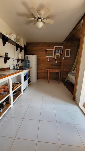 Una cocina compacta con ventilador de techo, armarios blancos y pared de madera.
