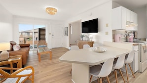 A modern kitchen with a flat-screen TV, white cabinets, and a dining area with a white table and chairs. - Villa Condo with Amenities and Short Beach Walk (Ocean City)