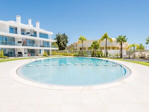 A modern building with a pool, surrounded by palm trees and a clear sky. - Apartment  by Interhome (Albufeira)
