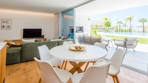 A modern living room with a large window, a flat-screen TV, a green sofa, and a dining area with white chairs and a round table. - Apartment  by Interhome (Albufeira)