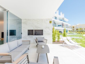Un espace de vie extérieur moderne comprenant un canapé, une table et des chaises, une cheminée et une vue sur un immeuble doté de balcons.